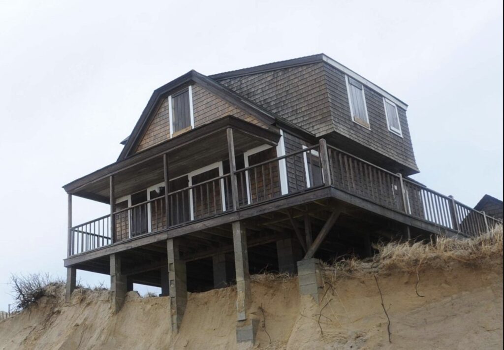 House on stilts above eroding sandy cliff
